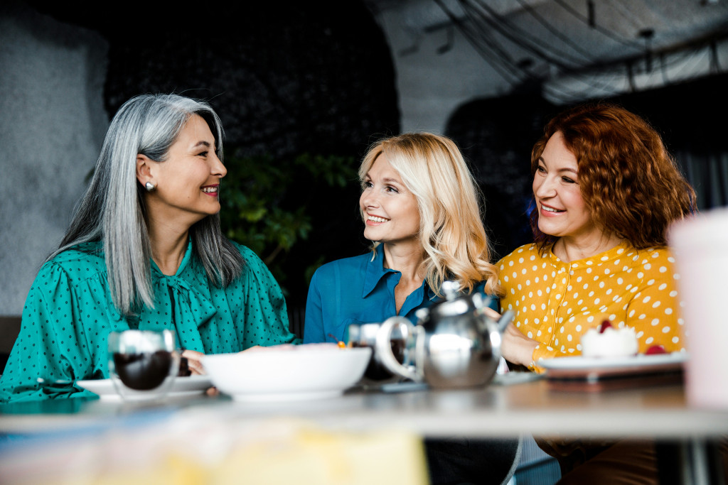 three women smiling and discussing perimenopause over coffee and tea