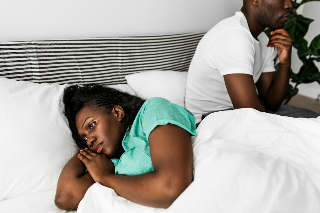 A woman lies in bed looking away from her partner with a pensive expression, representing the emotional strain and loss of connection that can occur due to low libido during perimenopause.