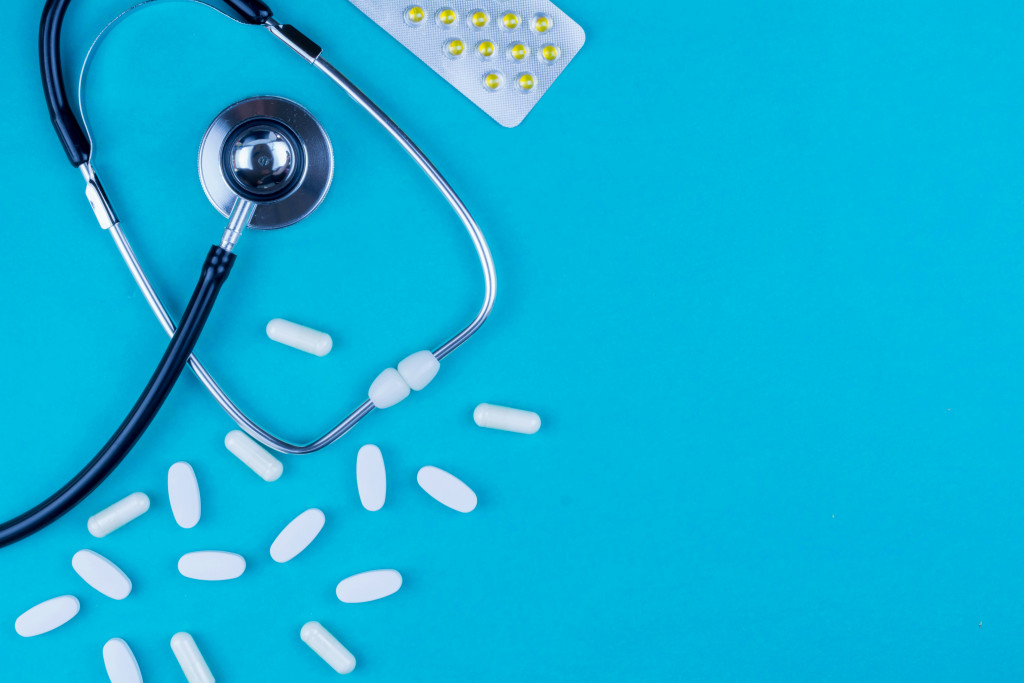 A stethoscope and various hormone medications are laid out on a clinical blue background, representing the medical evidence and prescribing protocols involved in testosterone therapy for women.