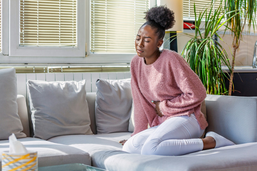 Women sitting on sofa holding her tummy while experiencing pelvic pain from endometriosis.